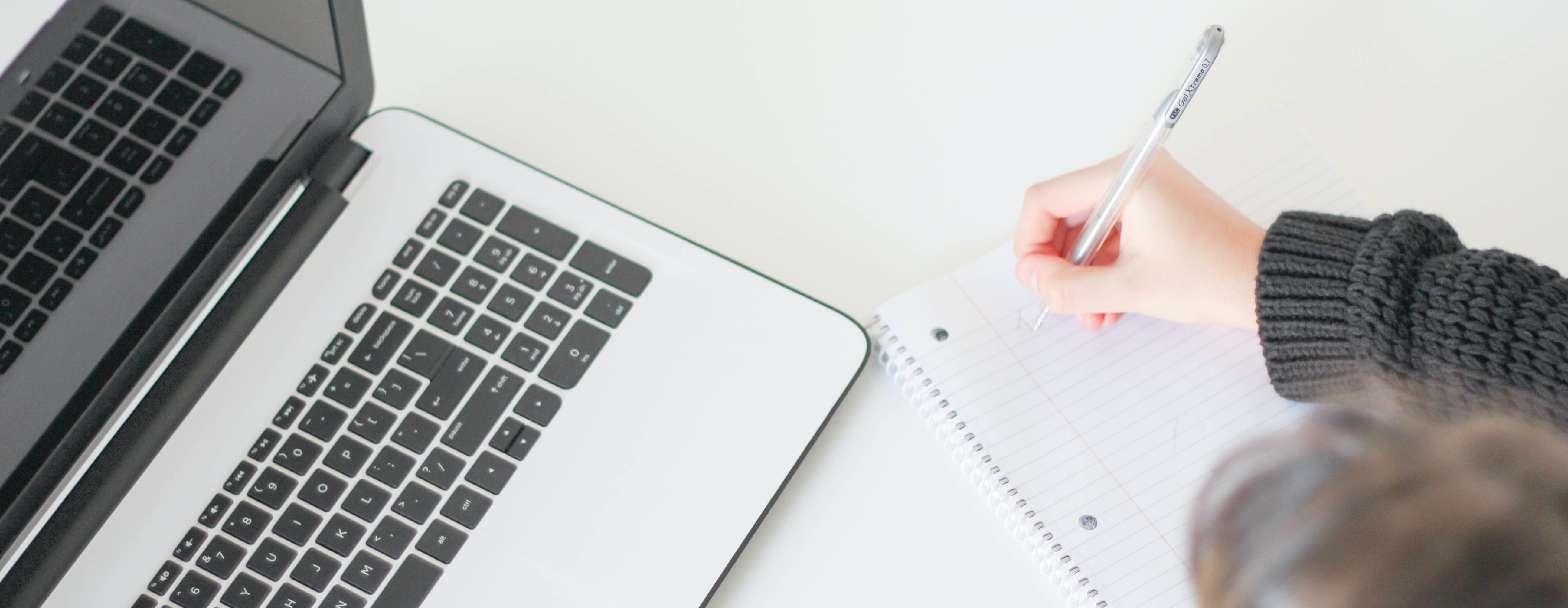 Person Writing Notes with Laptop Open